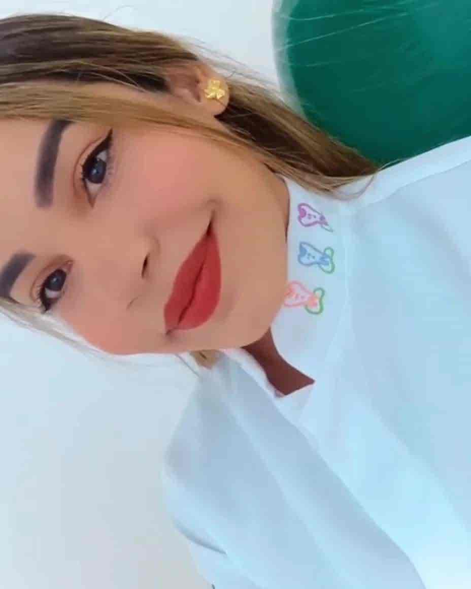 Denstista mulher sorrindo, de jaleco branco e cabelo preso.