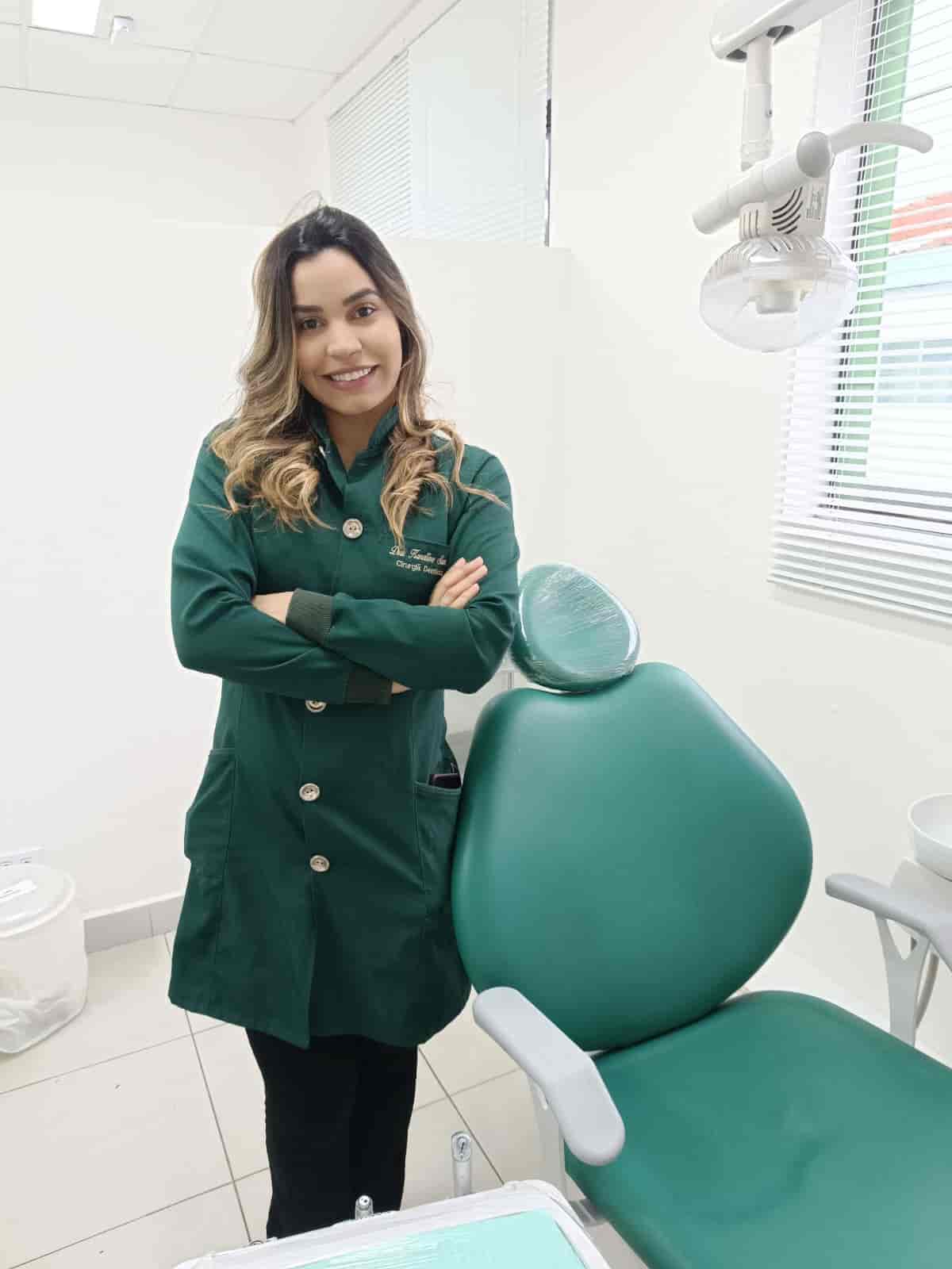 Dentista mulher em pé, com jaleco verde e sorrindo.